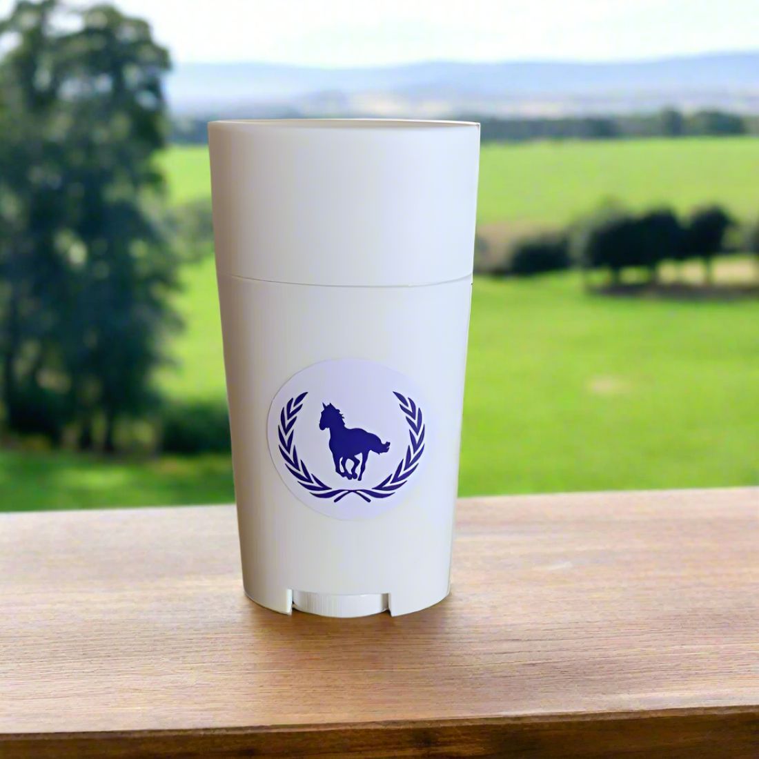 White leather conditioner container with a blue logo on a wooden surface with a green field and trees in the background